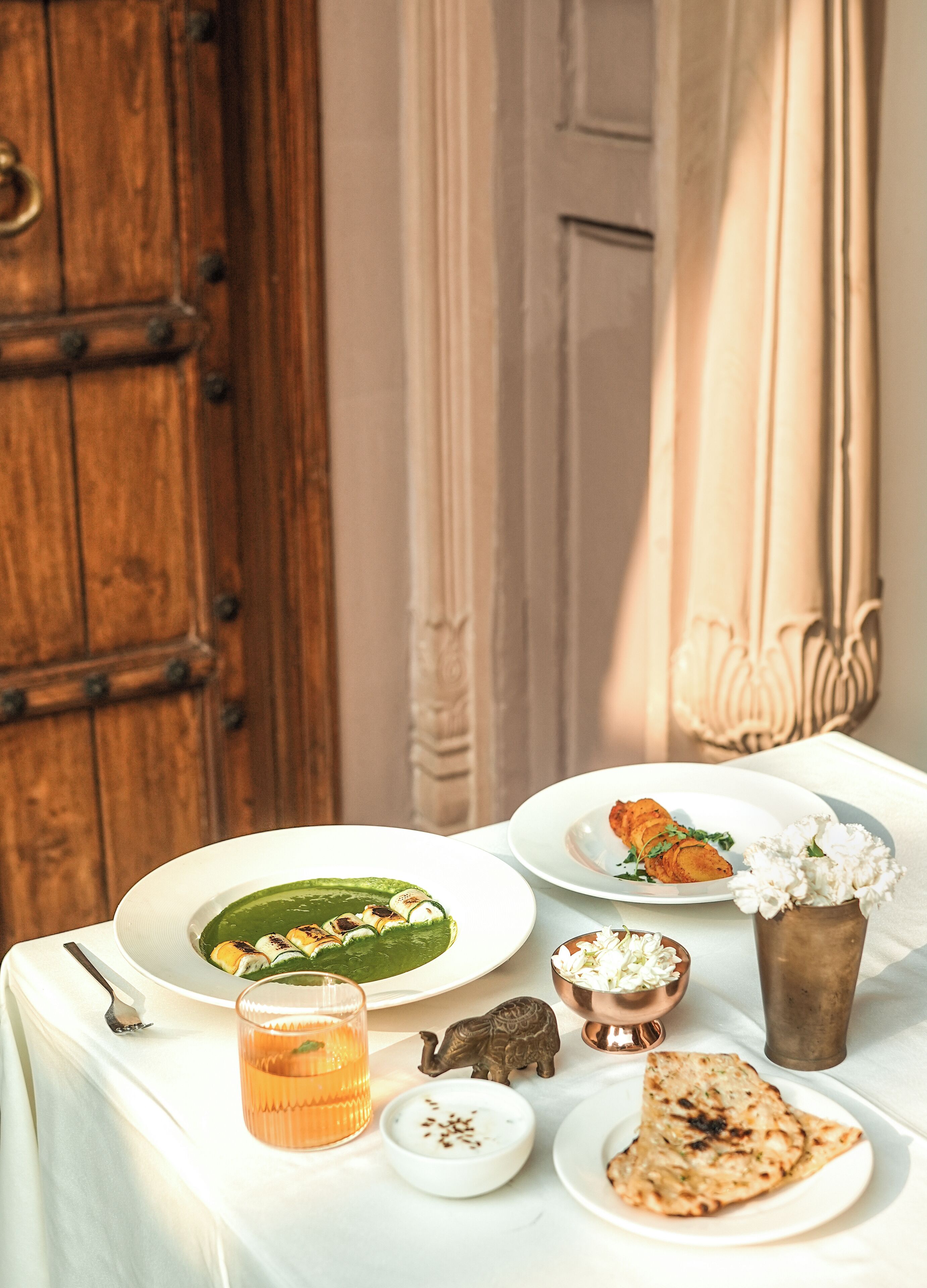 Ein Tisch, reichhaltig gedeckt mit verschiedenen Speisen, darunter ein Teller mit Essen, ein Glas Trank und eine kleine Schale Joghurt.