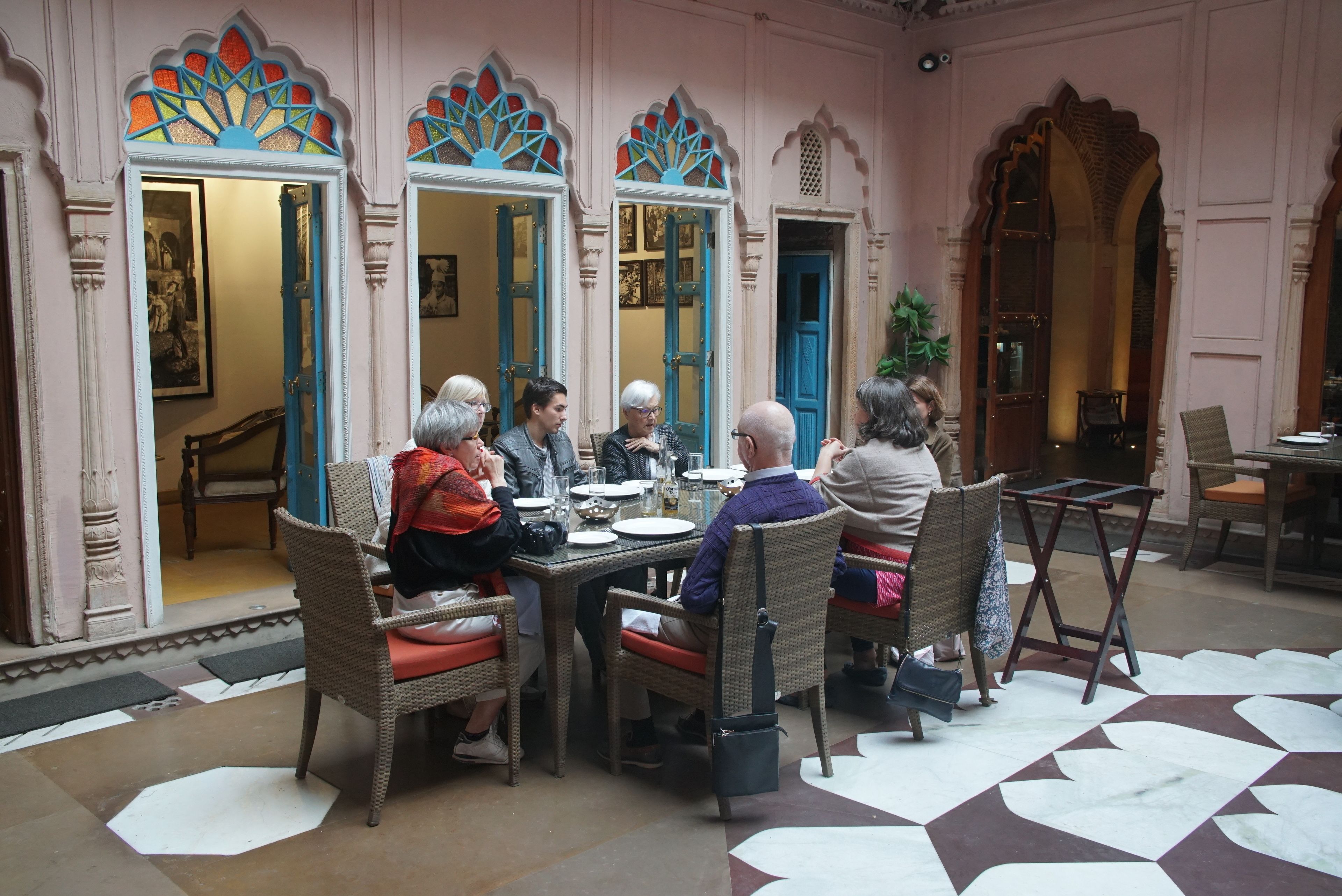 A group of people dining at a table with ornate mirrors and doors in a room with a patterned floor.