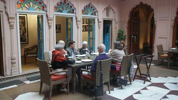 A group of people dining at a table with ornate mirrors and doors in a room with a patterned floor.