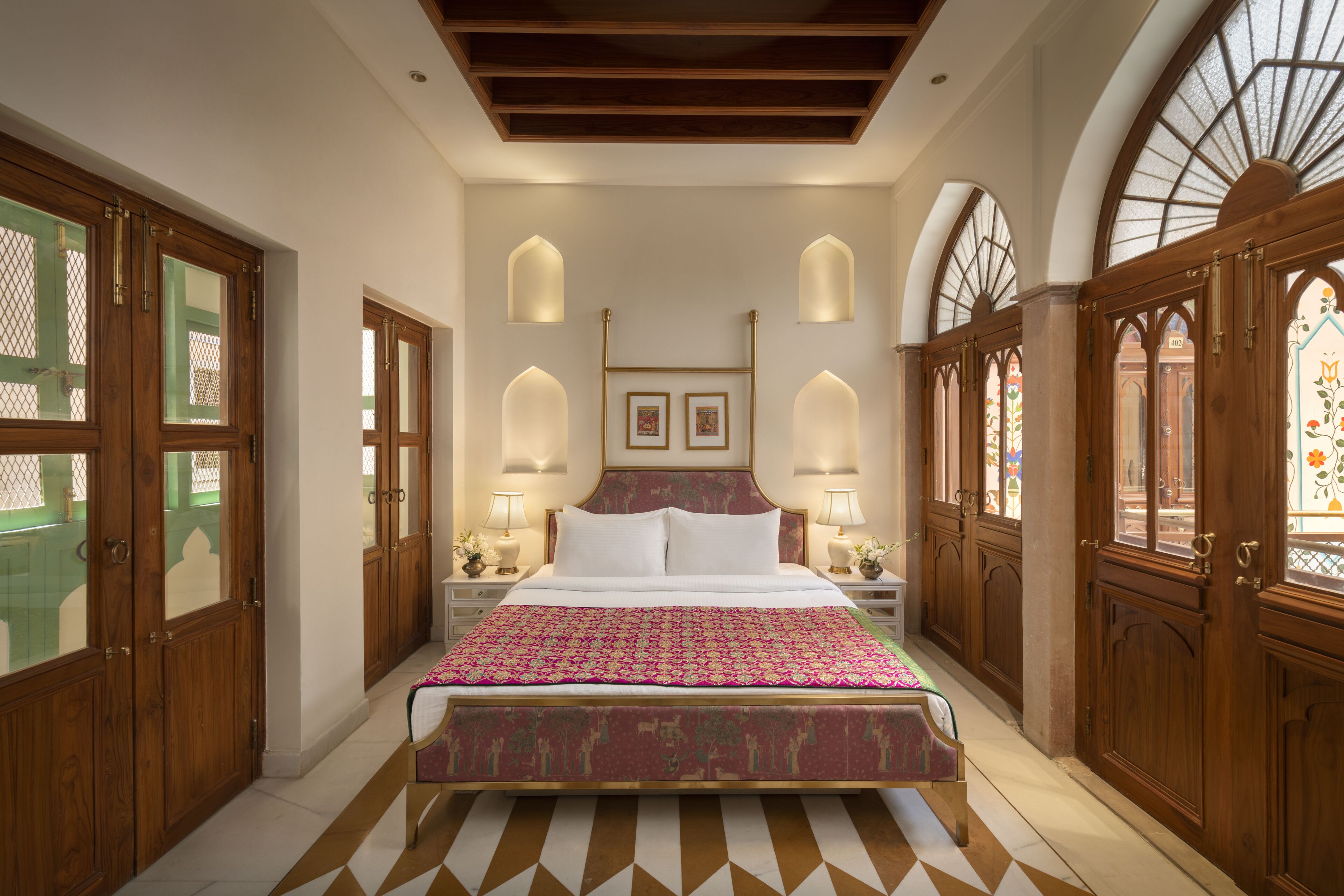 Ein Schlafzimmer mit einem großen Bett, Holztüren und Rundbogenfenstern.