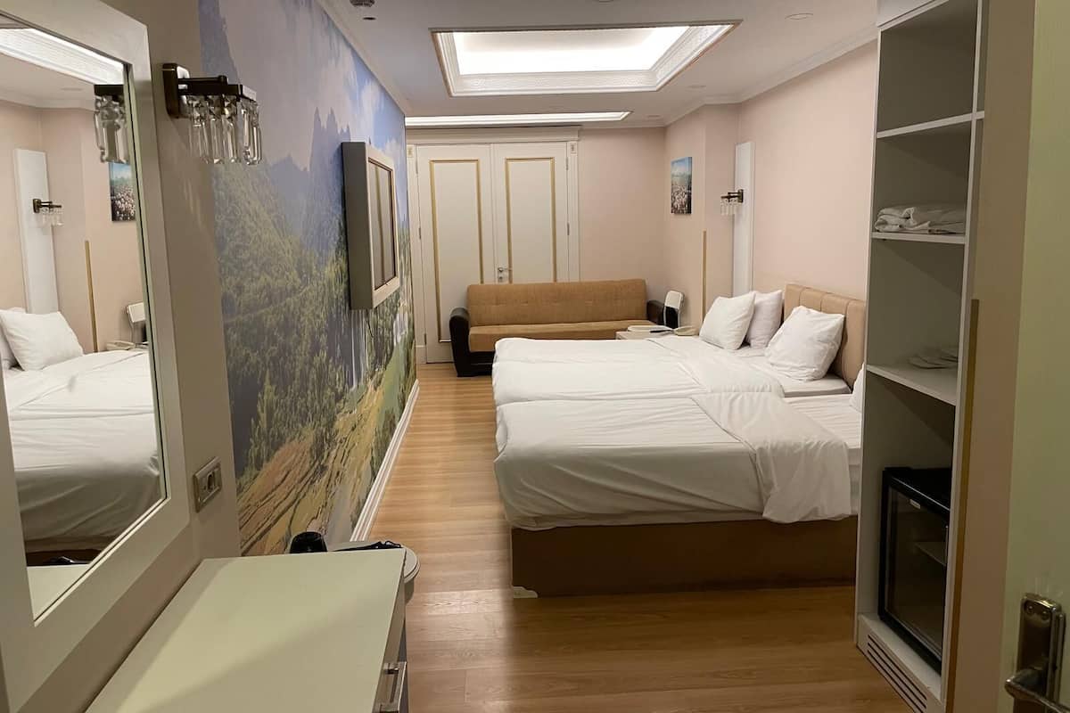 A hotel room with two beds, a sofa, a wardrobe, and a large mirror.