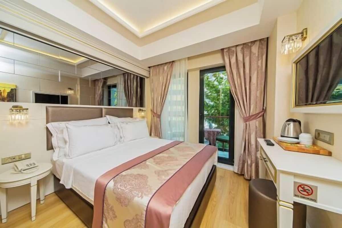 A hotel room with a bed, bedside table, desk, and a view of greenery outside.
