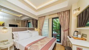 A hotel room with a bed, bedside table, desk, and a view of greenery. - Grand Naki Hotel (Istanbul)