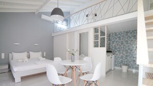 Une chambre à coucher moderne avec un lit, des tables de chevet, une table ronde blanche avec des chaises et un balcon doté d’une balustrade.