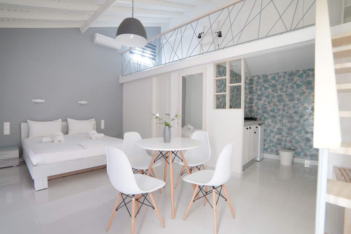 A modern bedroom with a bed, bedside tables, a white round table with chairs, and a balcony with a railing.