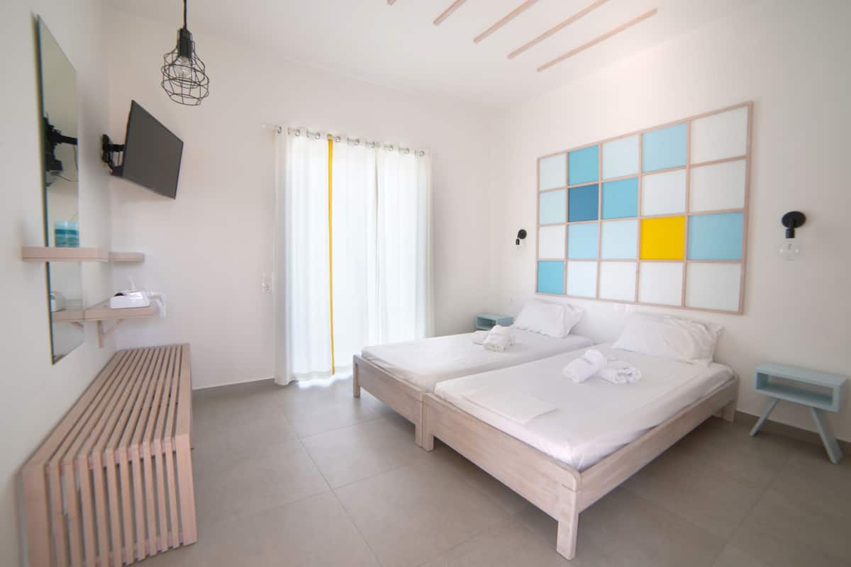 A hotel room with two beds, a large mirror, a TV, a bedside table, a bench, and a view of the outside.
