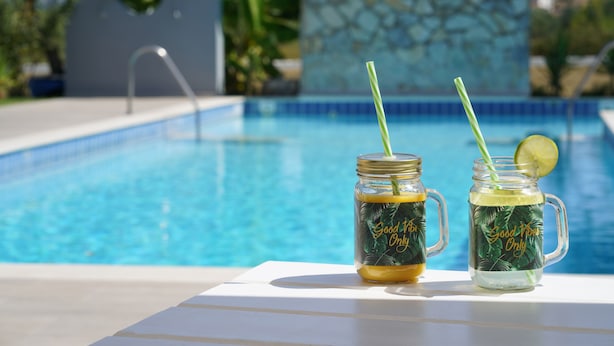 Deux bocaux en verre avec des pailles et une tranche de citron vert, étiquetés « Bonne humeur seulement », sur une table au bord de la piscine.