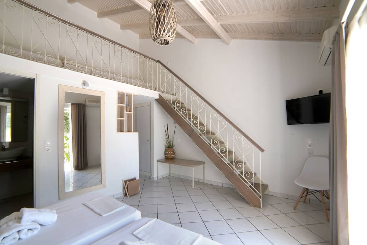 A hotel room with a large bed, a bathroom with a mirror, a staircase, and a television on the wall.