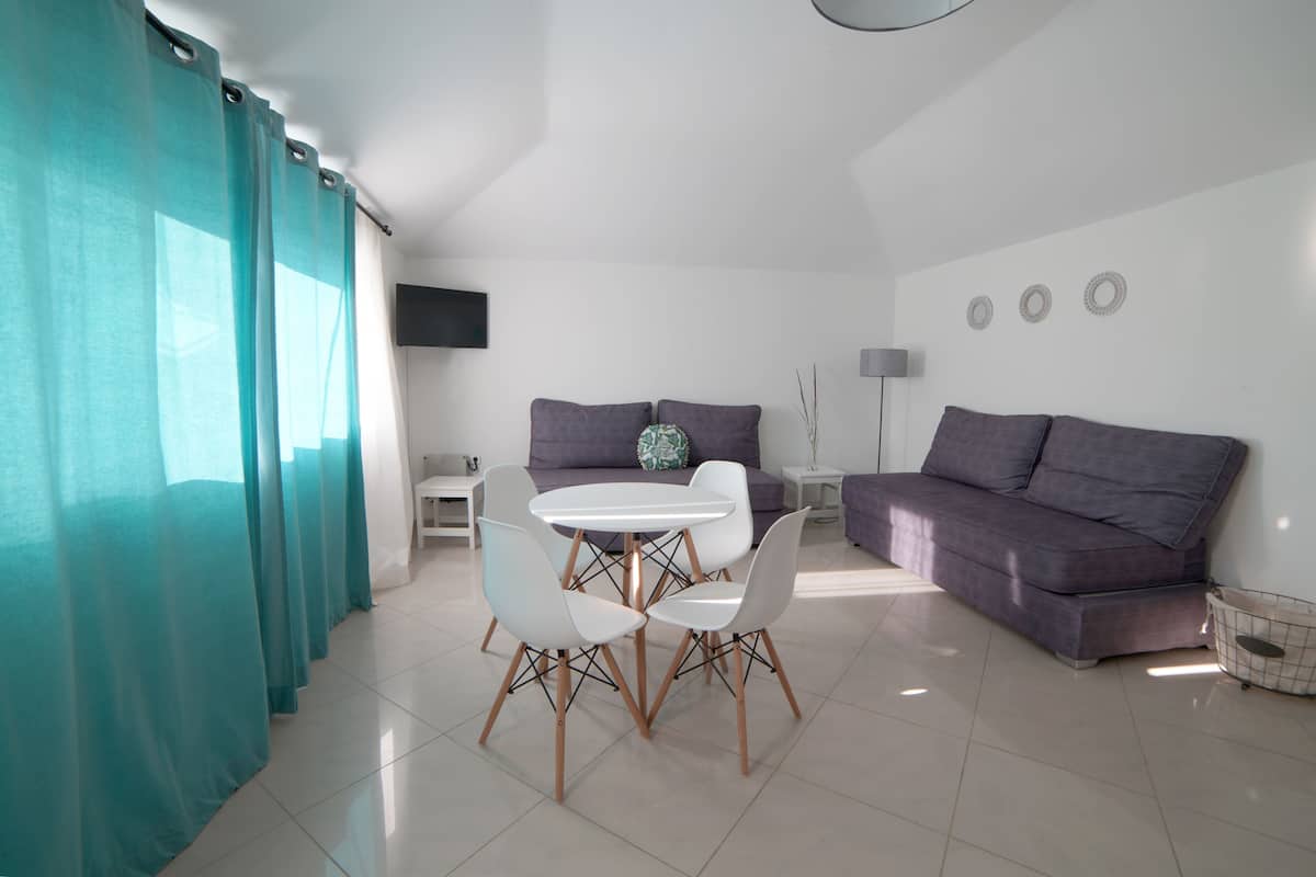 A modern living room with a dining area, a sofa, and a TV mounted on the wall.