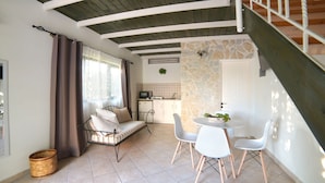 Un salon chaleureux avec un canapé, une table à manger et des chaises, une cuisine dotée d’un mur en pierre et un escalier.