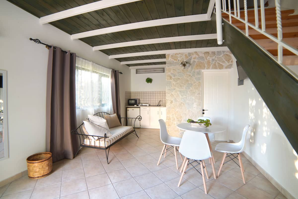 A cozy living area with a sofa, dining table, and chairs, a kitchen with a stone wall, and a staircase.