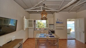 Cocina compacta con zona de comedor, televisor montado en la pared y vista al mar desde la ventana.