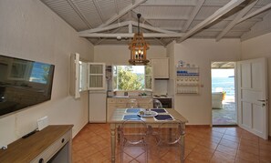 Une cuisine compacte avec un coin repas, un téléviseur fixé au mur et une vue sur la mer par la fenêtre.