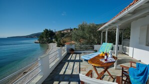 Una terraza con vista al mar, una mesa con una botella y fruta, y una silla con una toalla.