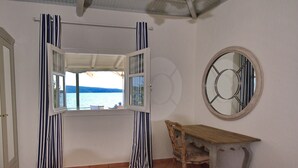 Un dormitorio con una cama, un banco de madera, un espejo redondo y una ventana con cortinas.