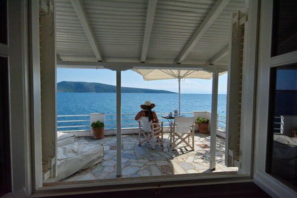 A covered outdoor seating area with a view of the sea and a mountain.
