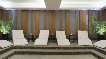 Un área de spa con cuatro sillones de descanso, dos plantas en macetas y dos mesitas con velas.