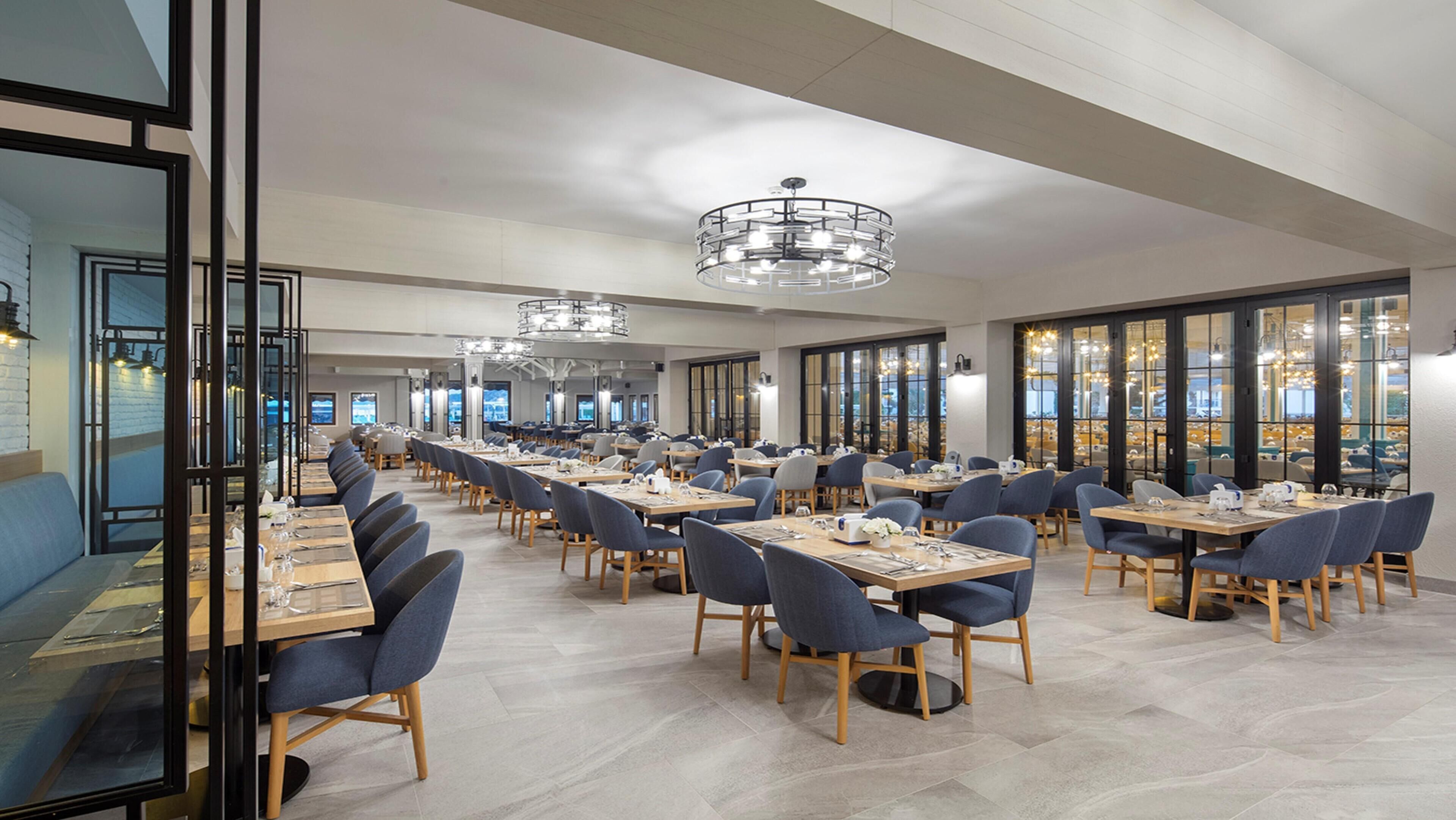 Un vaste espace dédié à la salle à manger, avec de nombreuses tables et chaises, de grandes fenêtres et des lustres modernes.