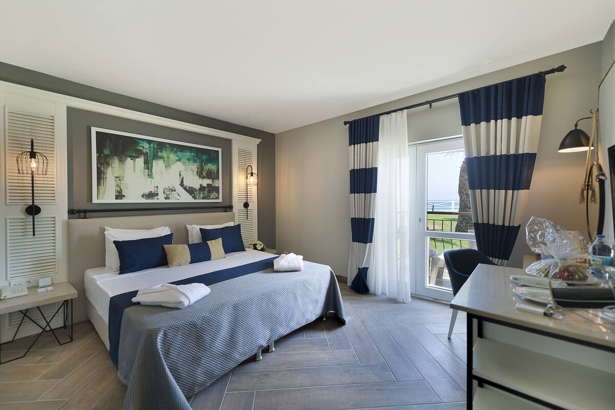 A hotel room with a large bed, a desk, a chair, and a balcony with curtains.