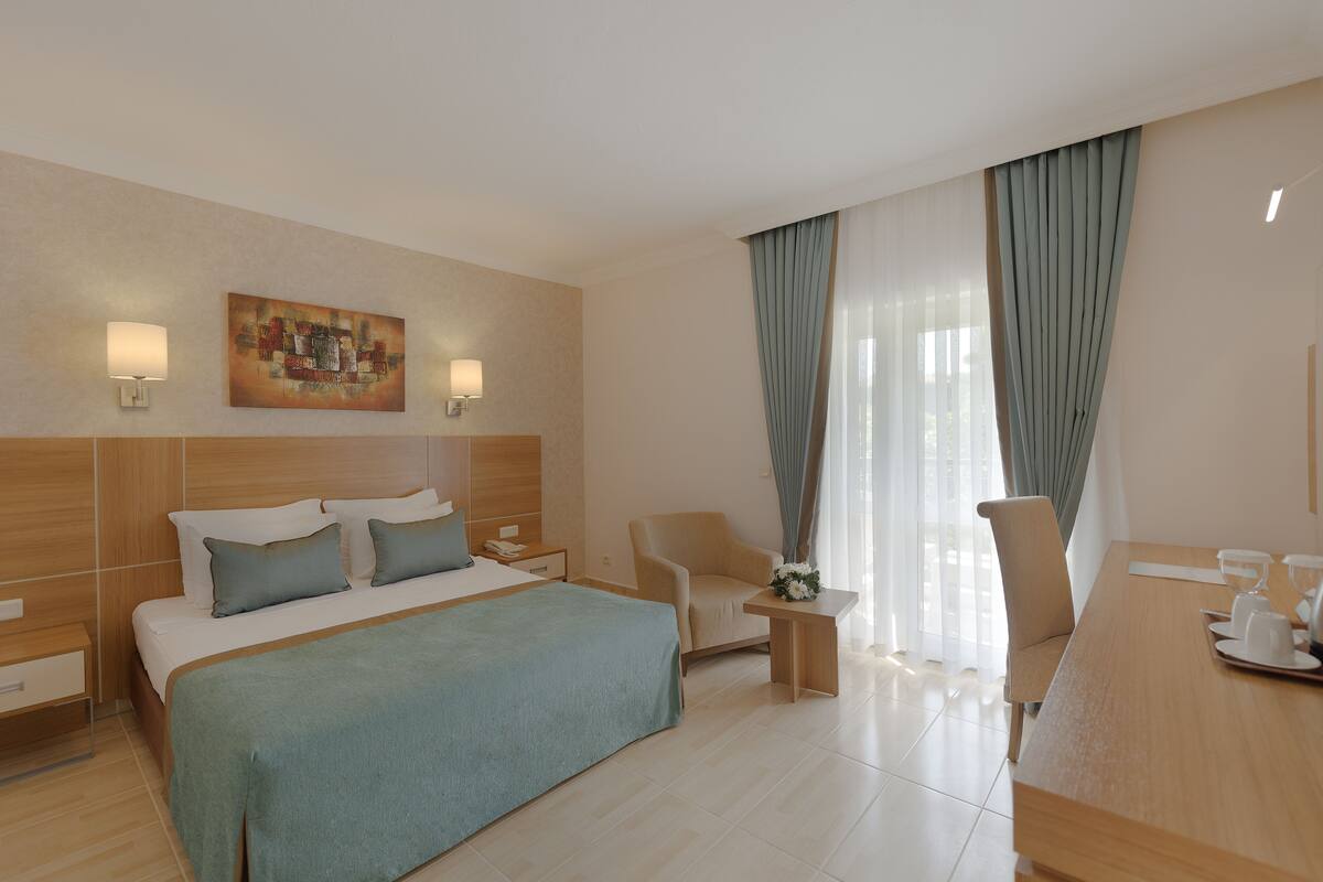 A hotel room with a bed, a desk, a chair, a nightstand, and a painting on the wall.