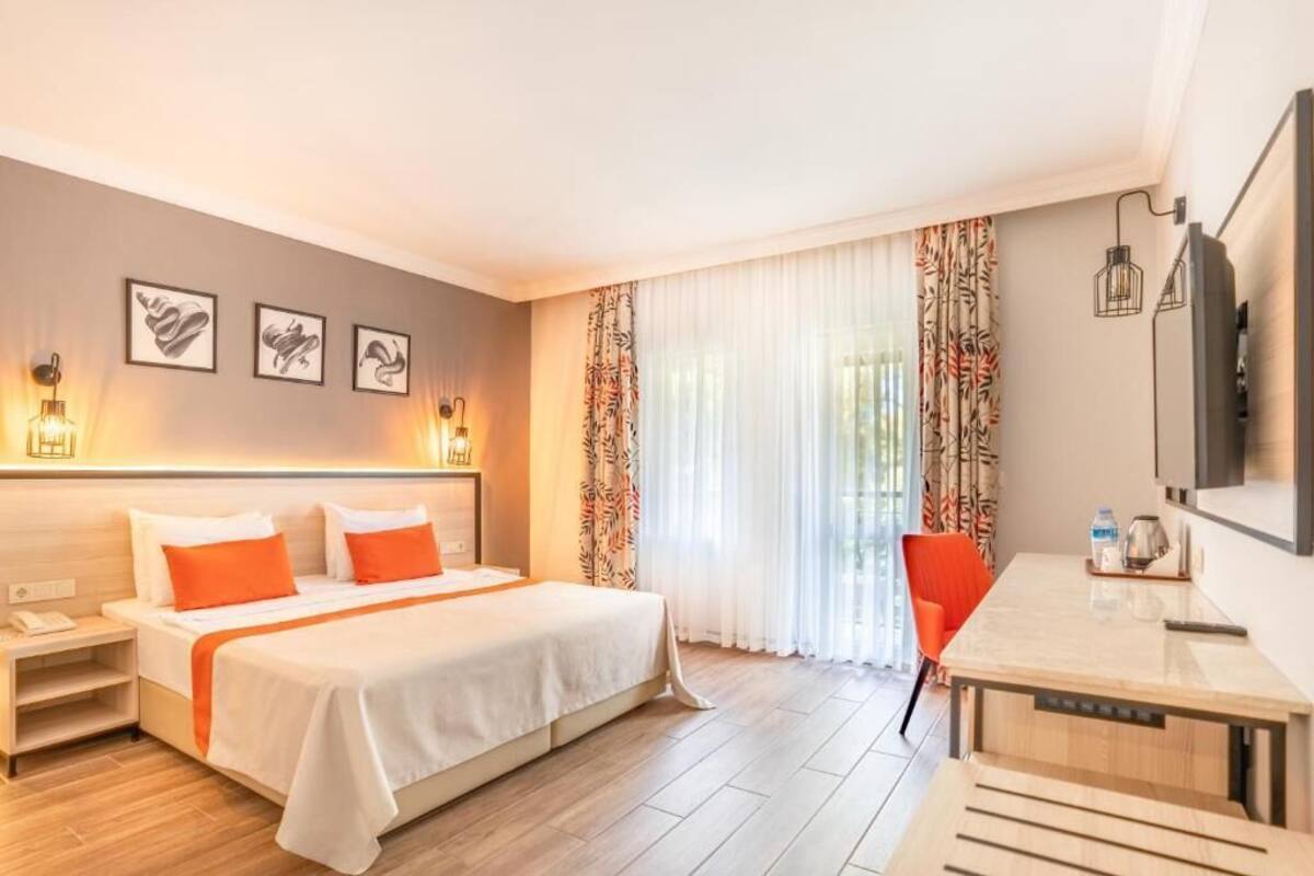 A hotel room with a bed, bedside table, chair, desk, and a TV.