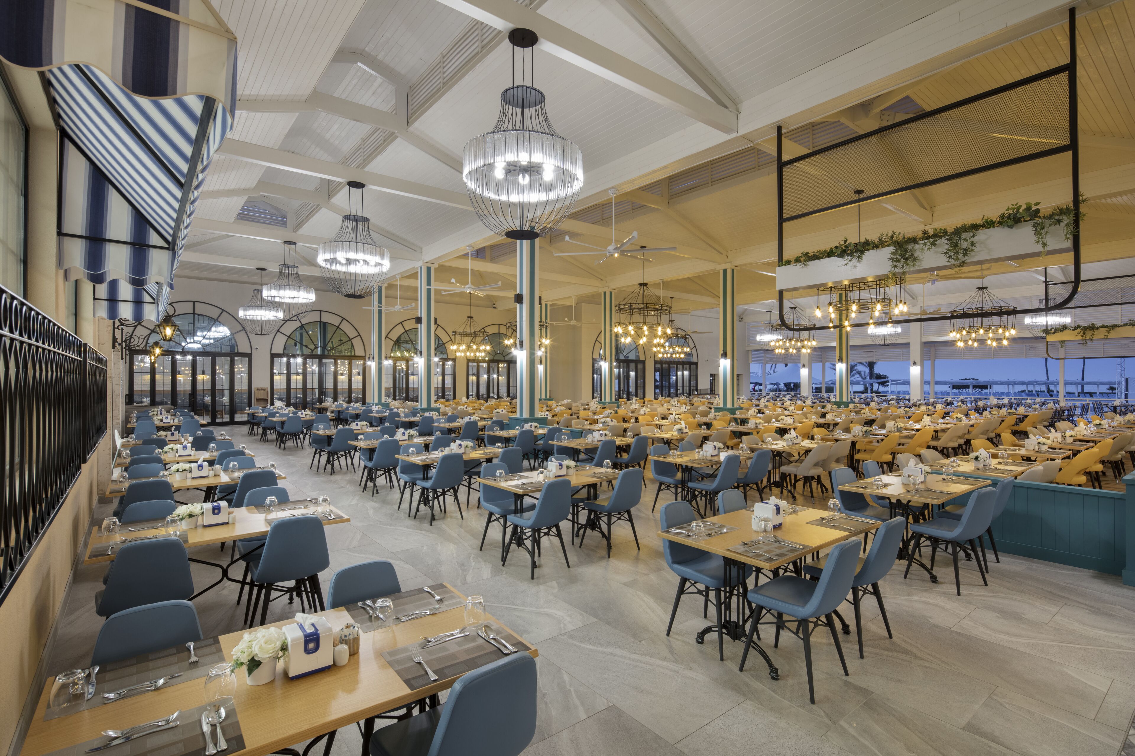 A spacious dining area with multiple tables and chairs, large windows, and decorative lighting fixtures.