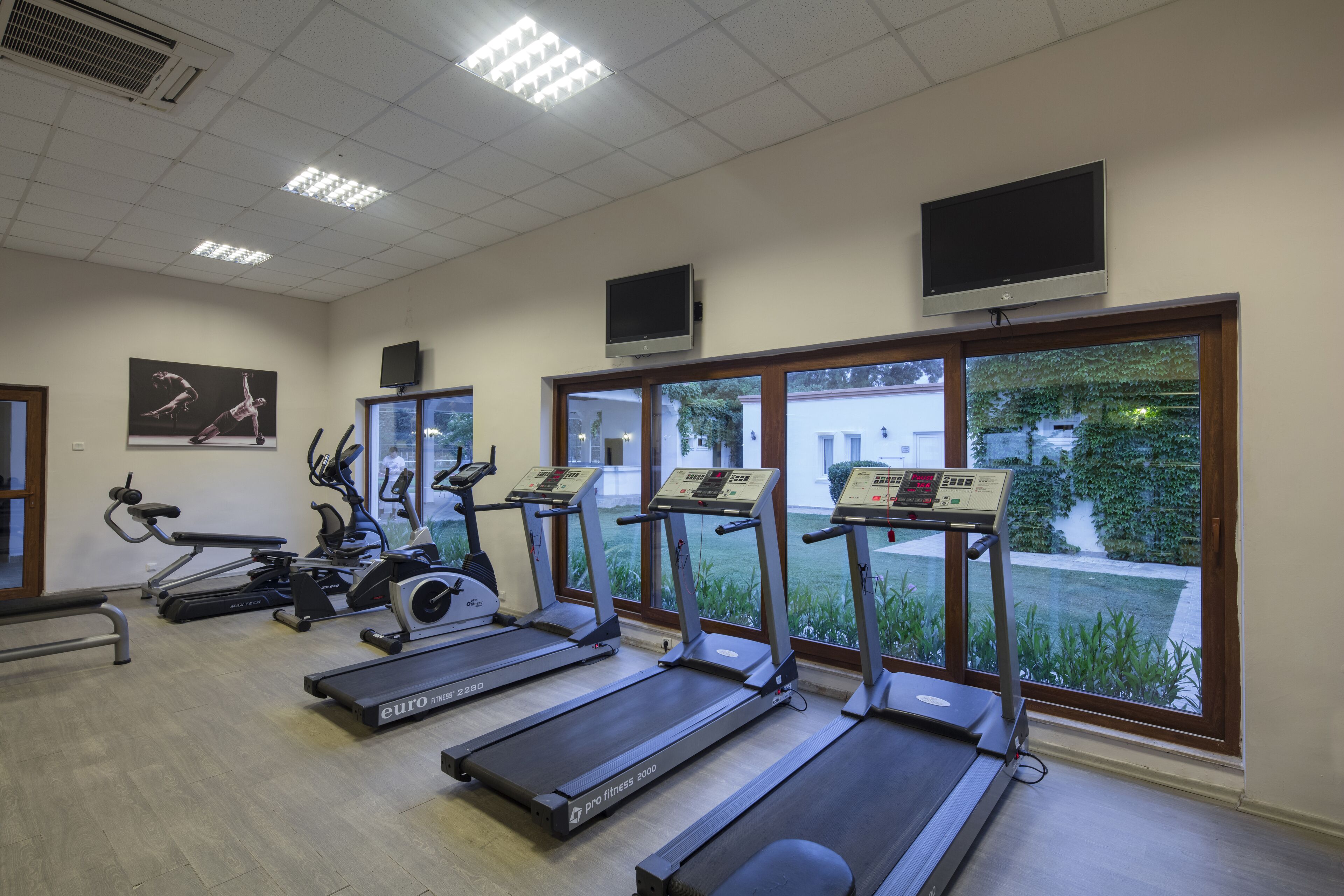 Ein Fitnessstudio mit Laufbändern, Crosstrainern und einer Bank.