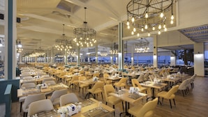 Un comedor amplio con varias mesas y sillas, ventanas grandes y lámparas modernas.