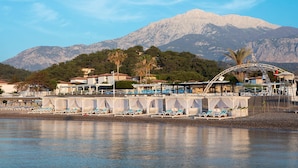 A coastal resort with beachside cabanas, a pool area, and a mountain backdrop. - Club Marco Polo - All inclusive (Kemer)