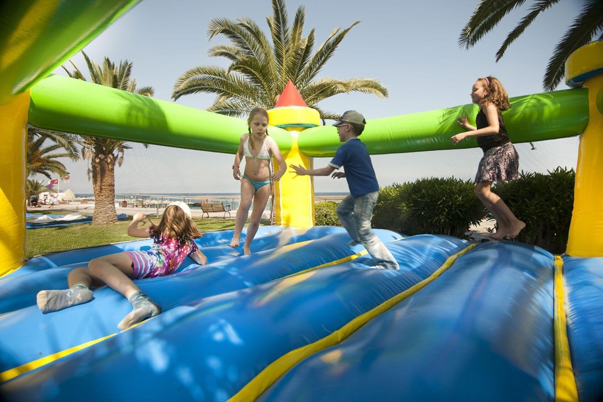 A group of people playing on a blue inflatable bouncy castle with a green and yellow structure in the background.