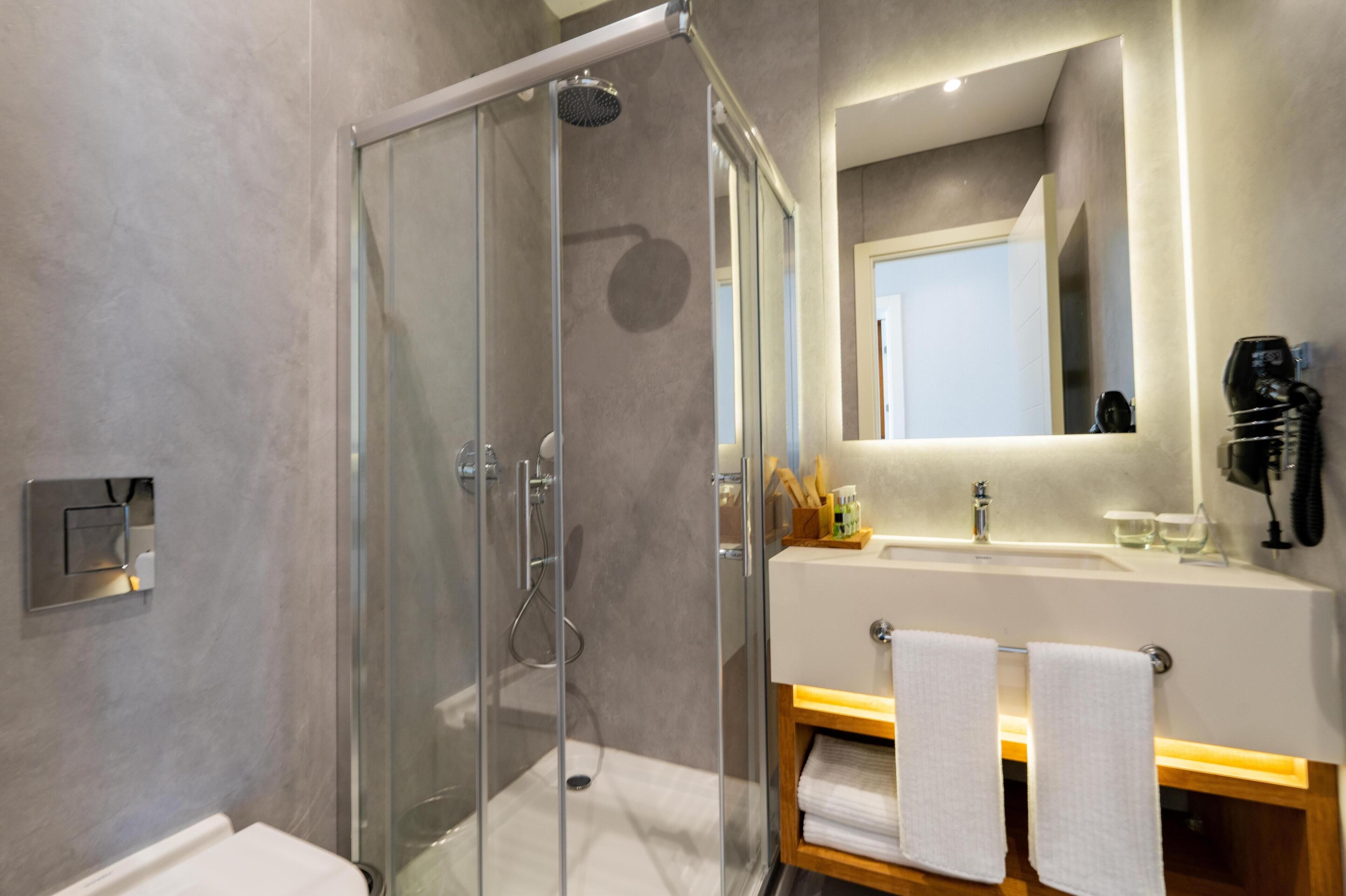 Un baño moderno con ducha de vidrio, tocador con espejo y perchero.