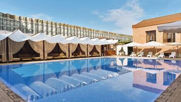 A swimming pool with lounge chairs and umbrellas, a brick building, and a fence with draped fabric.