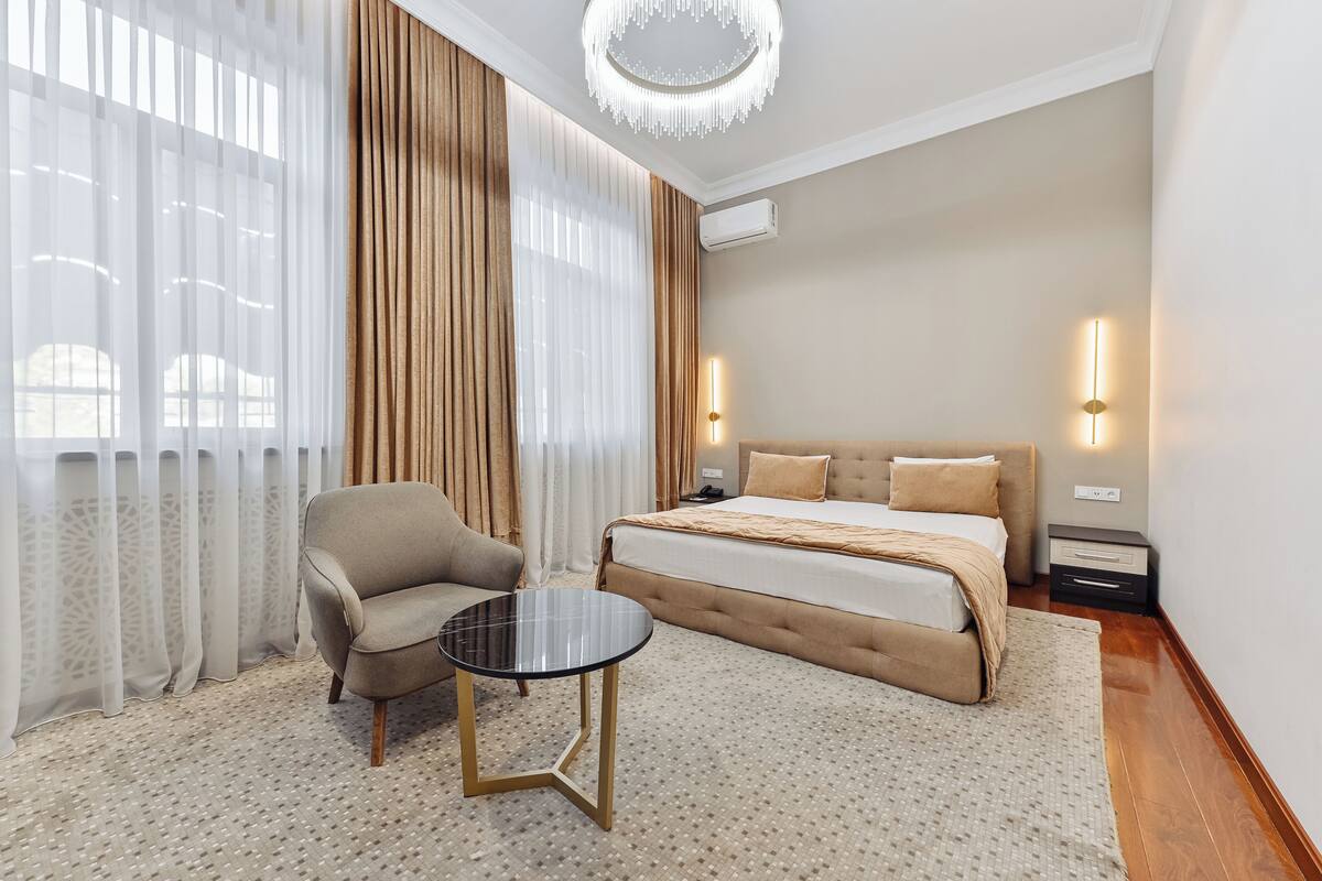 A bedroom with a bed, a chair, a small table, and a chandelier.