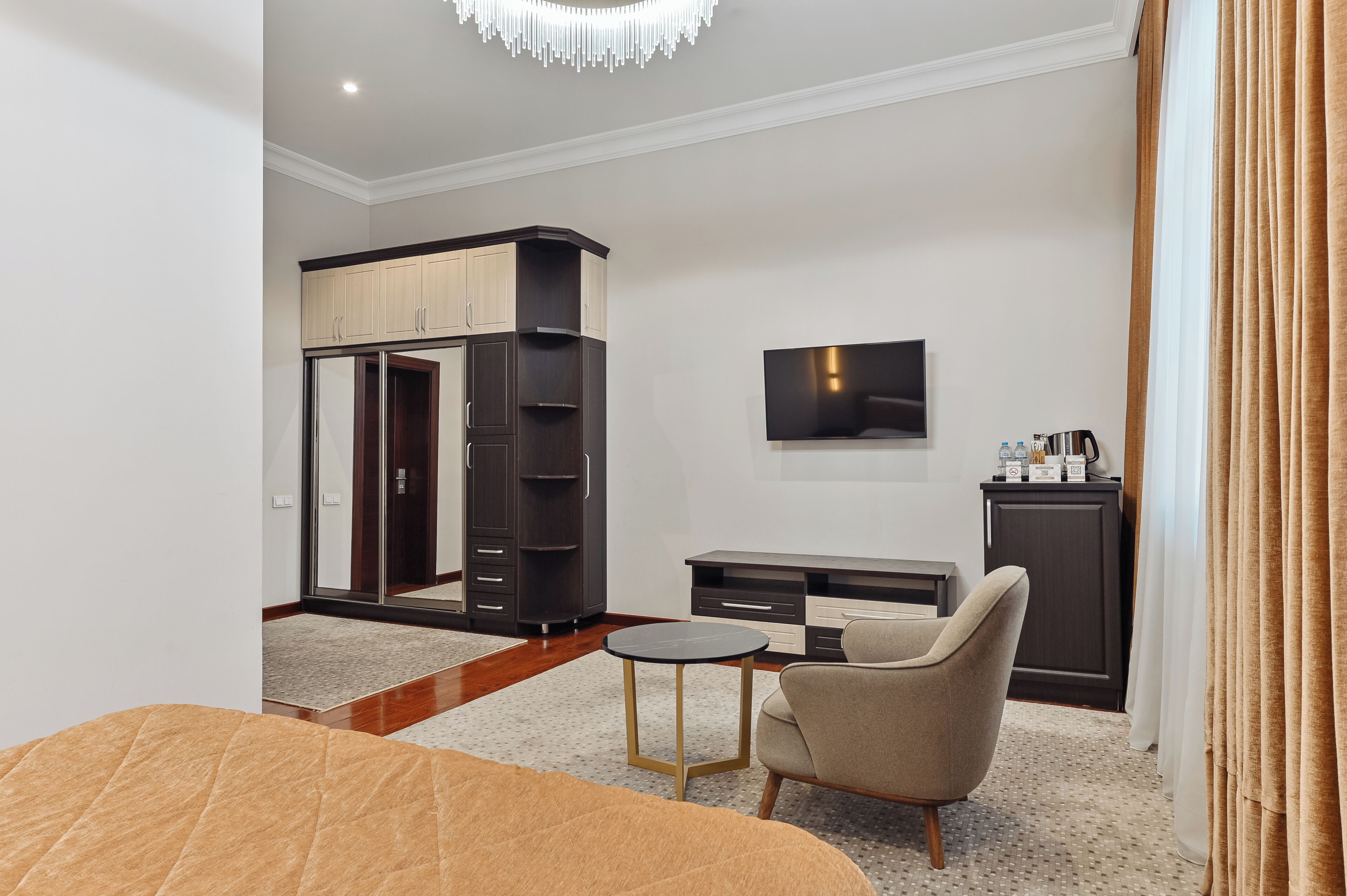 A modern hotel room with a bed, a TV, a small table, a wardrobe, and a desk.