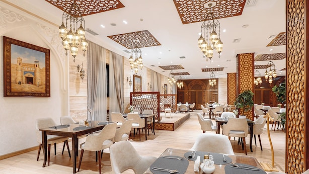 Un comedor amplio con varias mesas y sillas, diseños ornamentales en el techo y un cuadro grande en la pared.