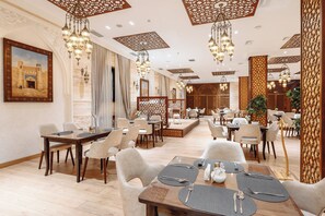A spacious dining area with multiple tables and chairs, ornate ceiling designs, and a large framed picture on the wall. - Ichan Qala Premium Class Hotel (Tashkent)