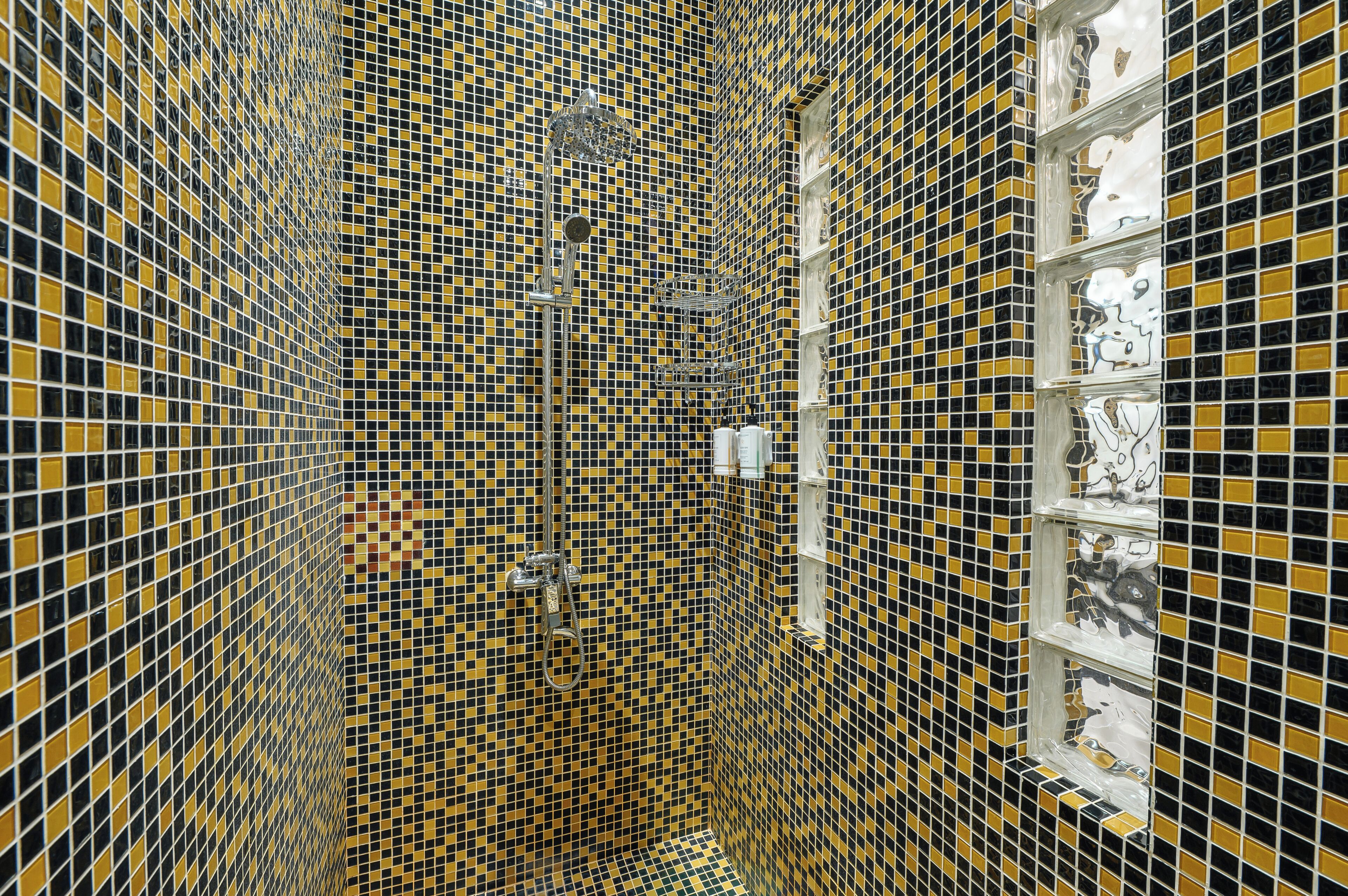 A bathroom with a checkered tile pattern, a shower, and a shelf with decorative items.
