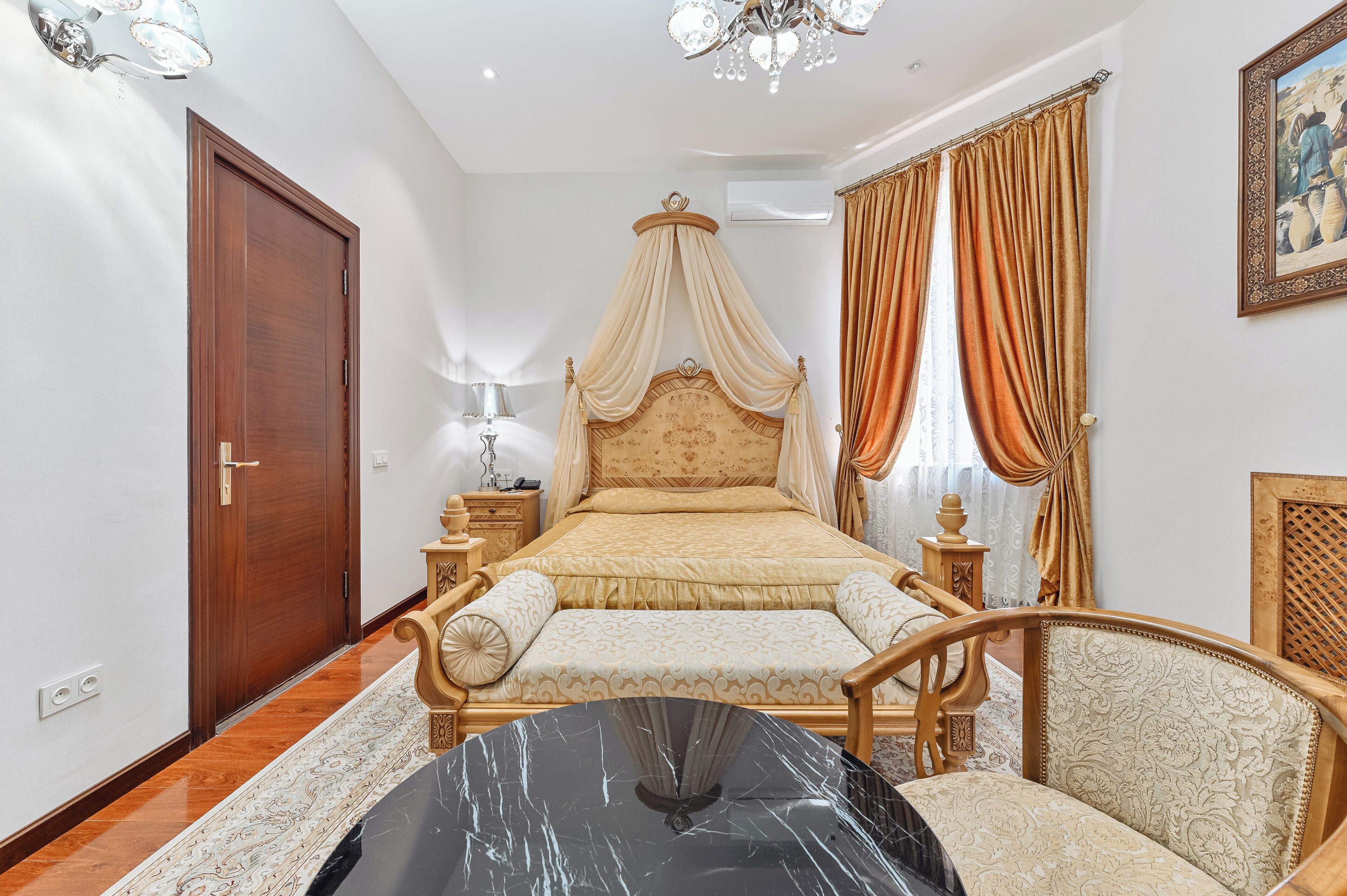 Un dormitorio con cama con dosel, puerta de madera, mesita de noche, lámpara y una silla.