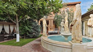 Un patio con una fuente, estatuas, un edificio de ladrillo y mesas al aire libre.