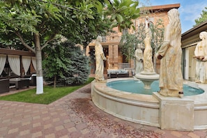 A courtyard with a fountain, statues, a brick building, and outdoor seating. - Ichan Qala Premium Class Hotel (Tashkent)