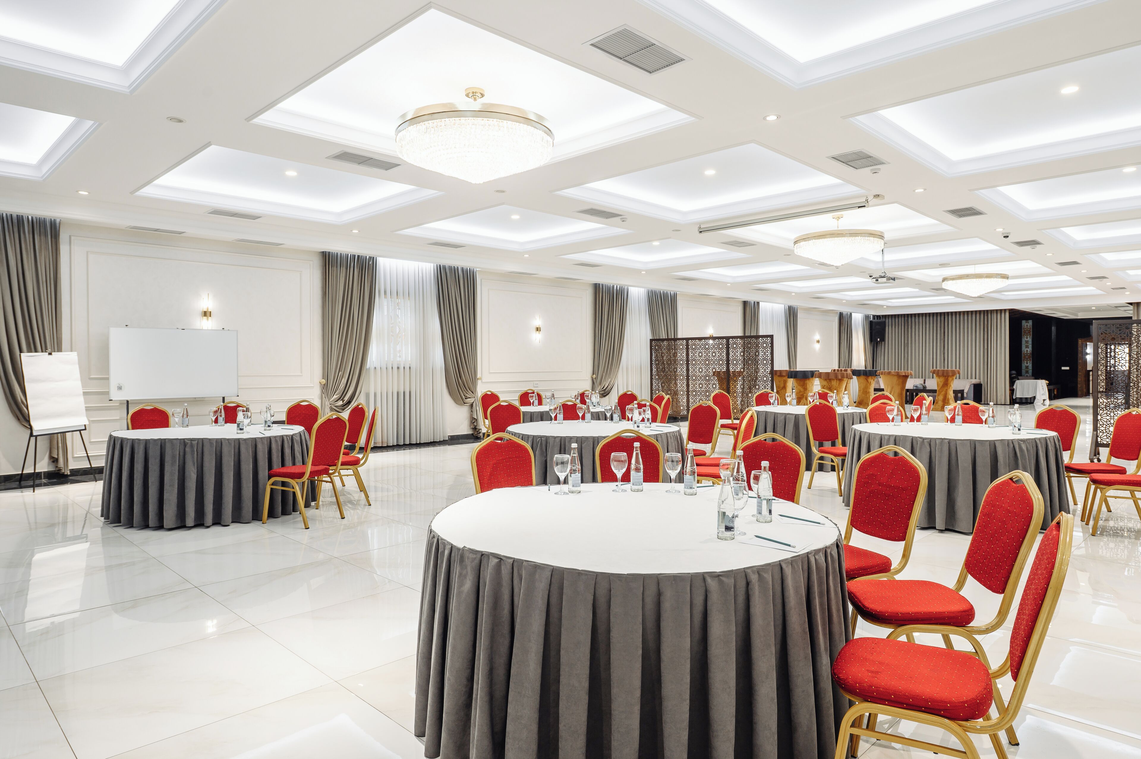 A conference room with multiple round tables, red chairs, and a whiteboard.