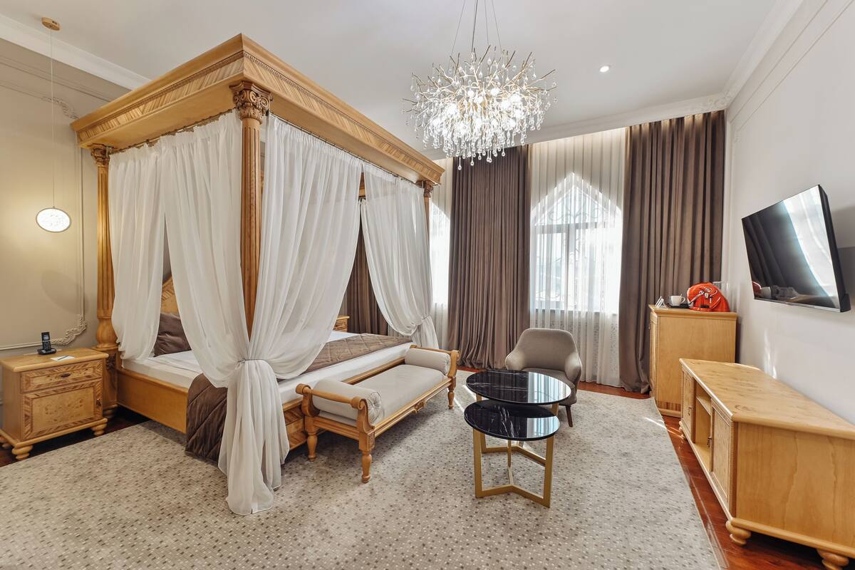A four-poster bed with a canopy, a round black table, a television on the wall, and a wooden nightstand.