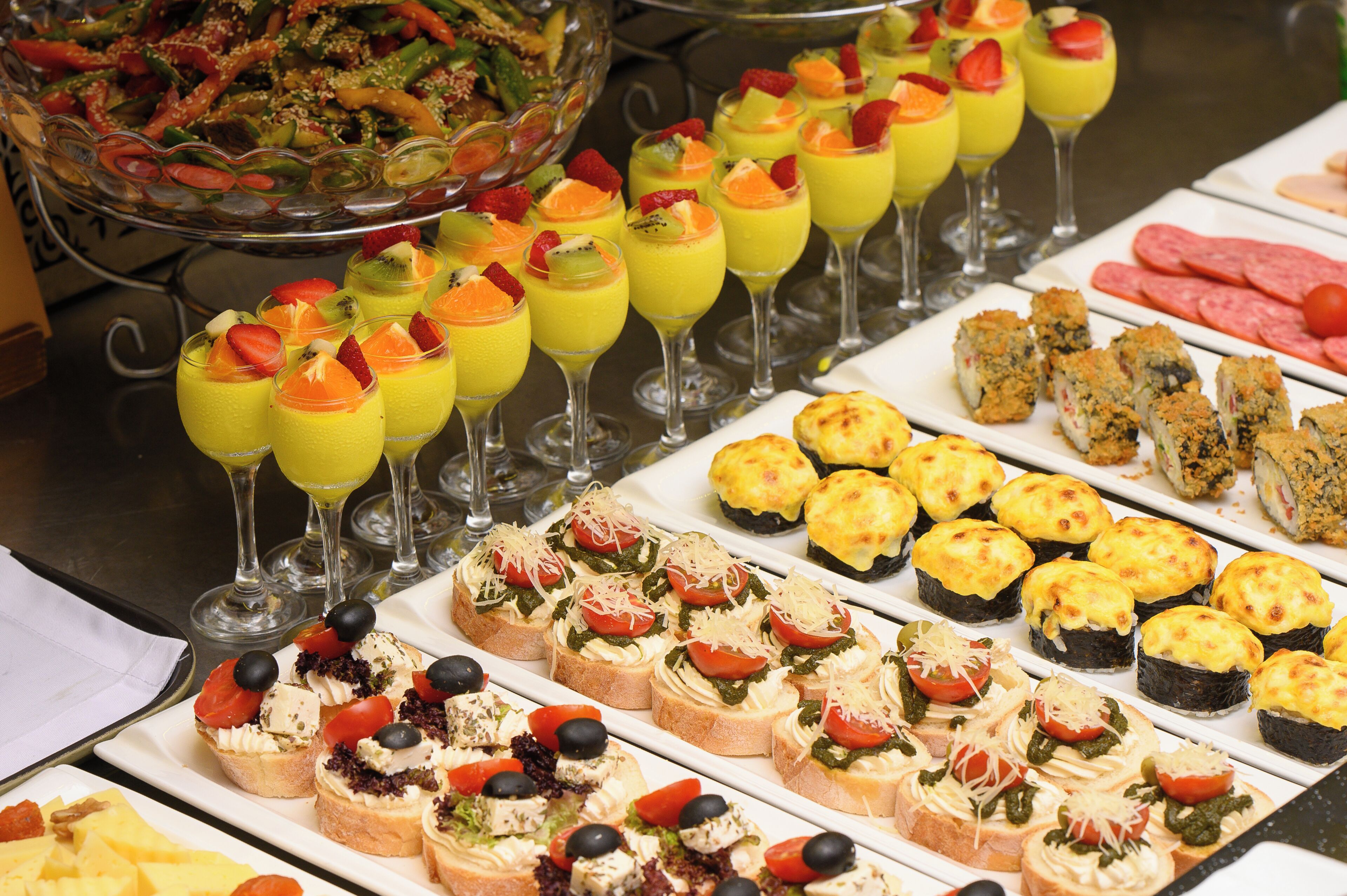 A buffet with various food items including fruit cups, sushi, and appetizers.