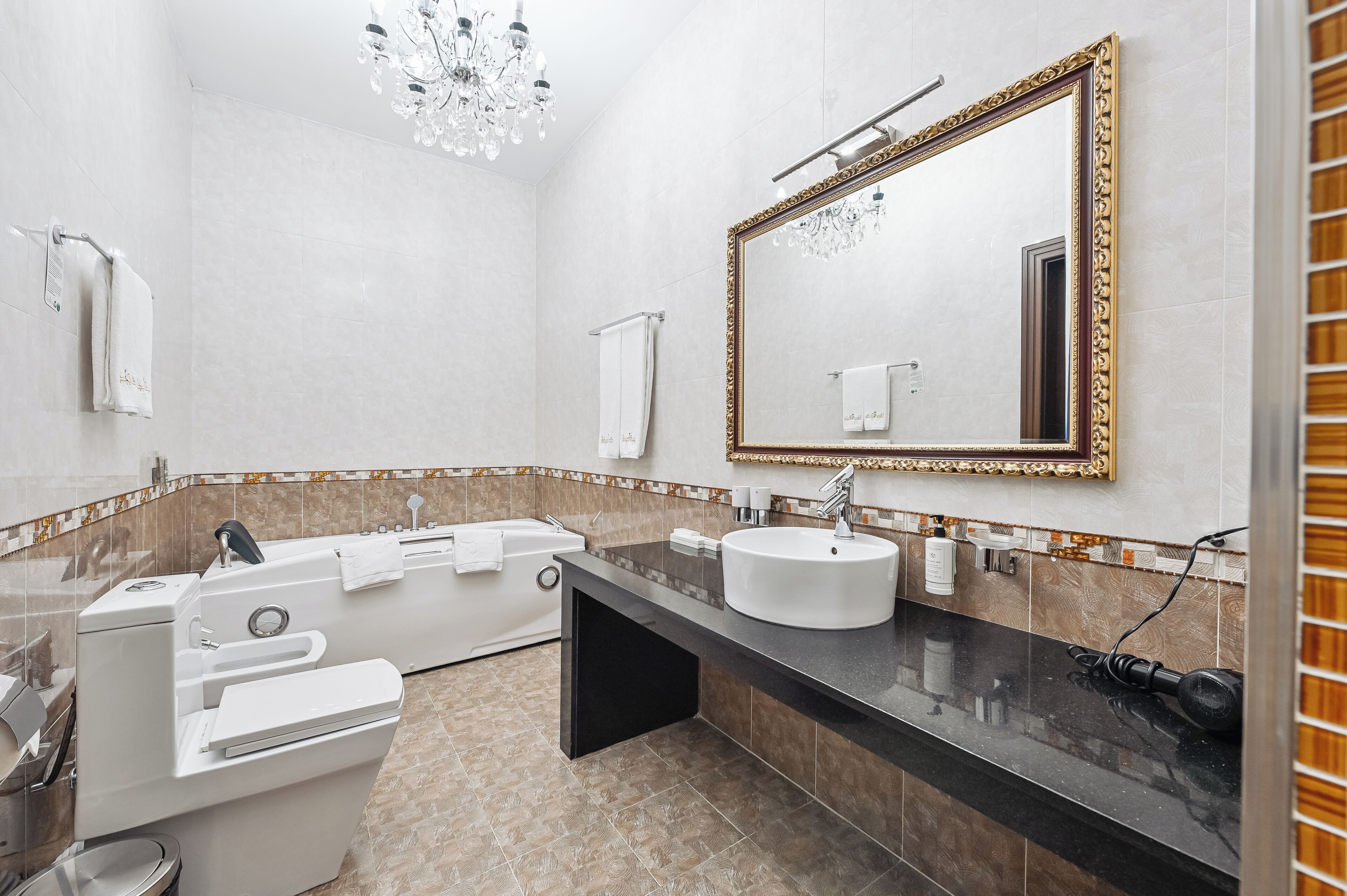 Une salle de bain moderne avec une baignoire, un meuble-lavabo, un grand miroir et un lustre.
