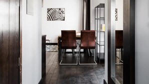 A modern interior with a dark wooden floor, a dining area with leather chairs, and a bookshelf.