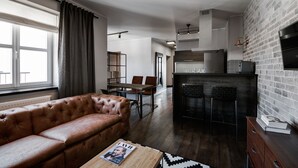 A modern living room with a leather sofa, a dining area, and a kitchen with a brick wall.