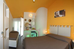A hotel room with a bed, a desk with a computer, a small fridge, and a mirror.