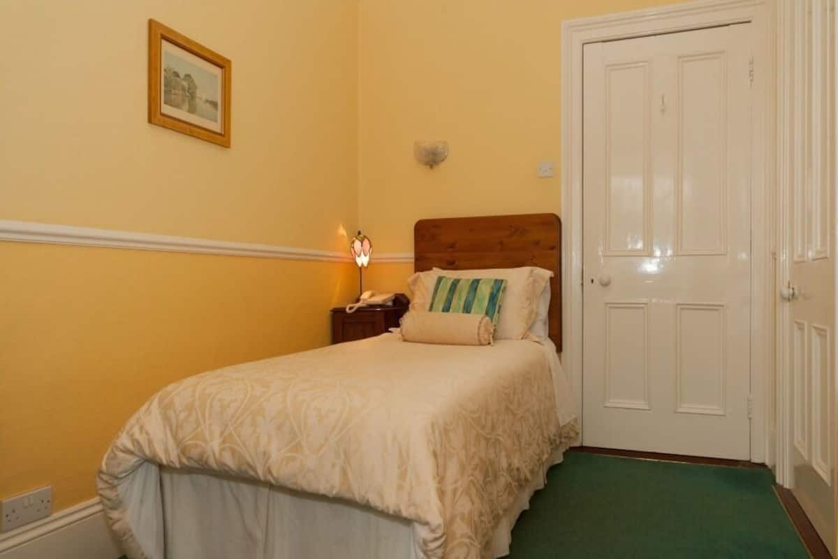 A bedroom with a bed, a nightstand, a lamp, a door, and a wall-mounted picture.