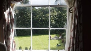 A window with a view of a well-maintained lawn and trees, curtains with a pattern, and a small decorative item on the window sill. - Ivyleigh House (Portlaoise)
