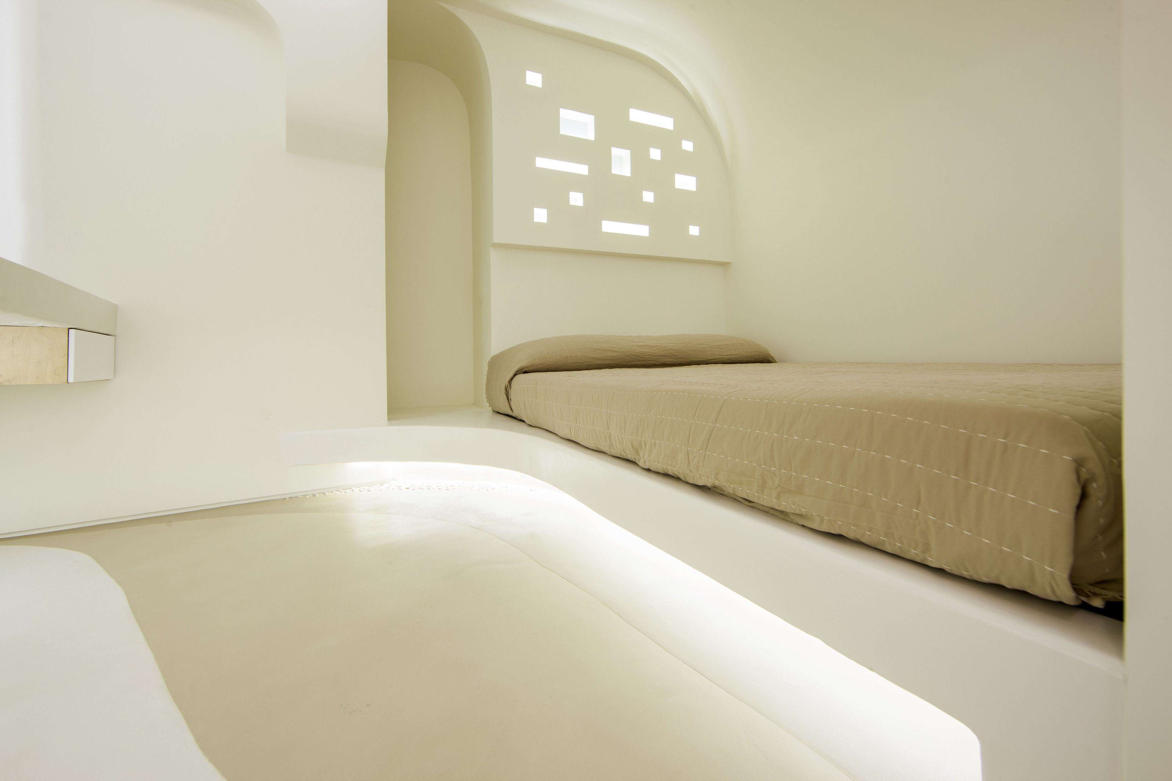 Ein schlicht eingerichtetes Zimmer mit einem Bett, einem kleinen Tisch und einer Wandleuchte.